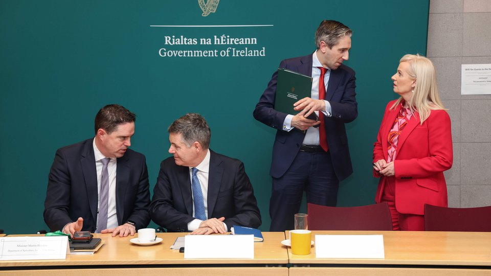 four people in suits talking in twos at a meeting