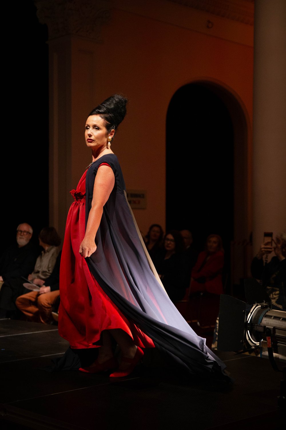 A model on the runway wearing a red dress with a black cape
