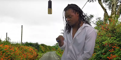 man in white shirt with microphone hanging above with Irish road projected behind him